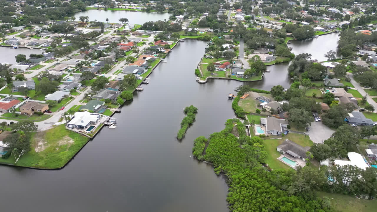 Canal area with green water, small docks, and surrounding suburban homes, aerial approach to homes