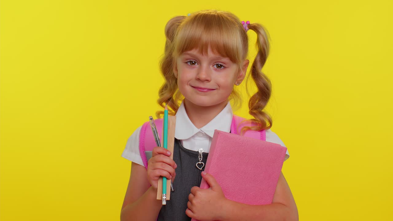 Ragazza di scuola allegra e divertente con libri vestita in uniforme indossa uno zaino sorridendo guardando la telecamera