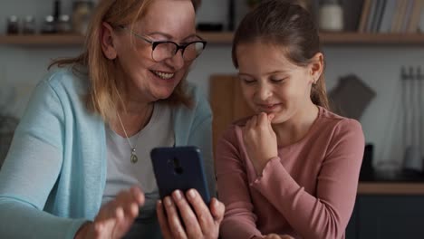 Caucasian-grandmother-and-granddaughter-using-mobile-phone-in-the-kitchen