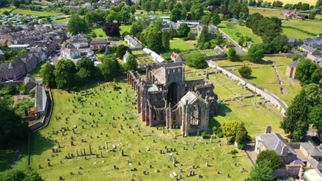 Stunning-aerial-pan-around-historic-Scottish-landmark-Melrose-Abbey,-small-town-in-Scottish-countryside-with-national-heritage