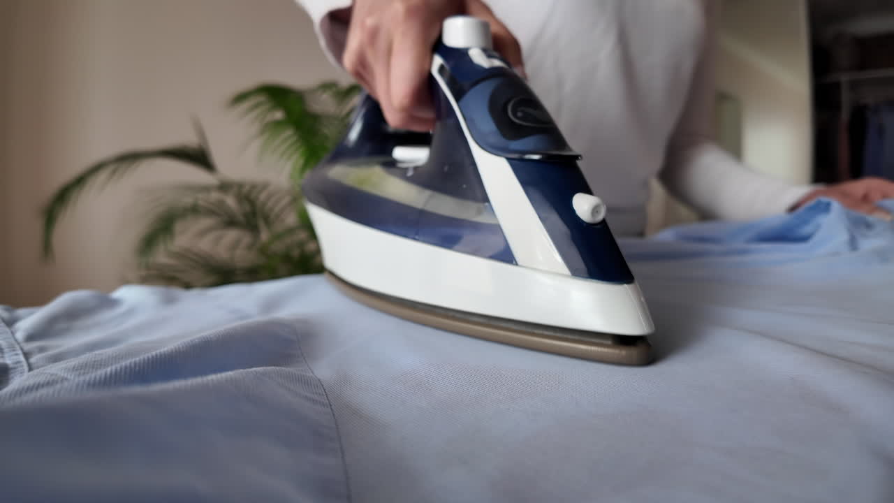 Close up woman ironing a blue shirt at home with white steam