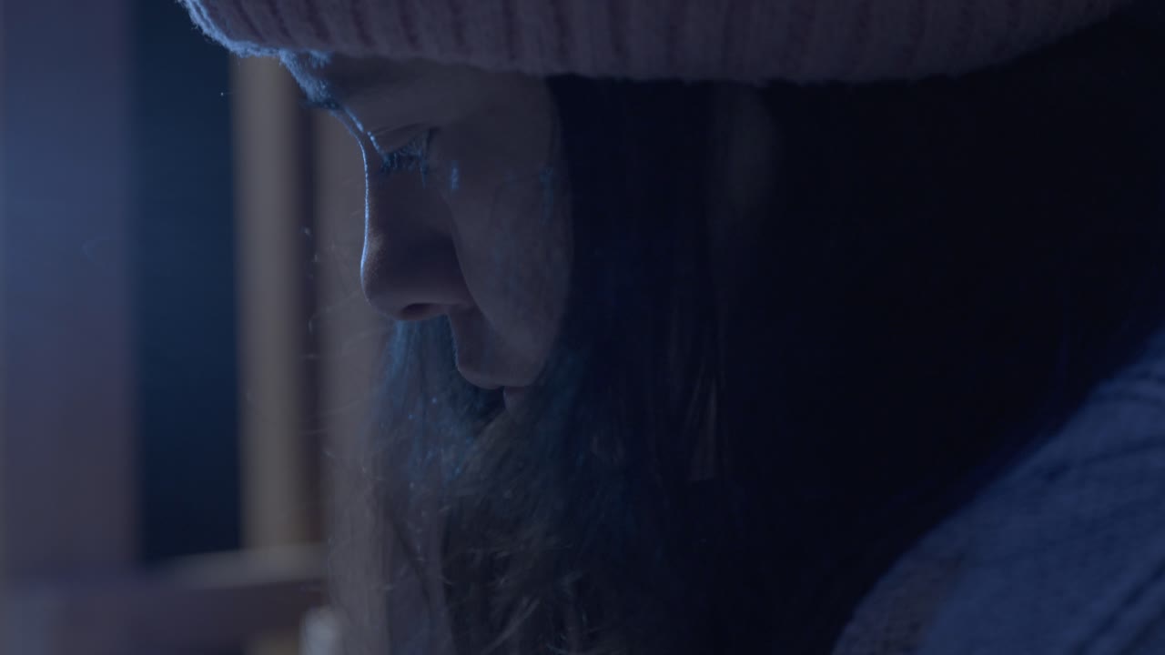 Close-up de uma garota em um quarto aconchegante embrulhando um presente, usando um gorro de tricô sob luz baixa e quente, criando uma atmosfera íntima e focada com texturas ricas e sombras suaves.