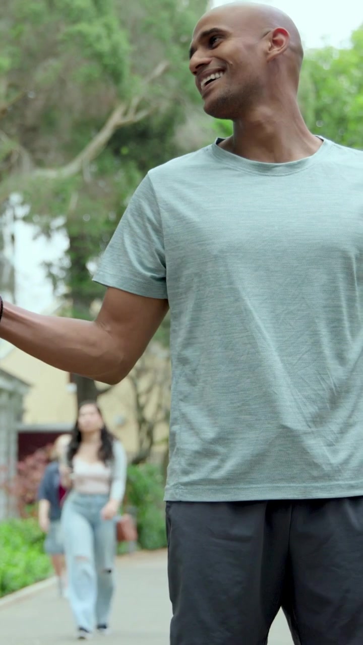 Video verticale: Corridore ansimante in pantaloncini che controlla lo smartwatch per il ritmo dopo aver superato il partner nel parco.
