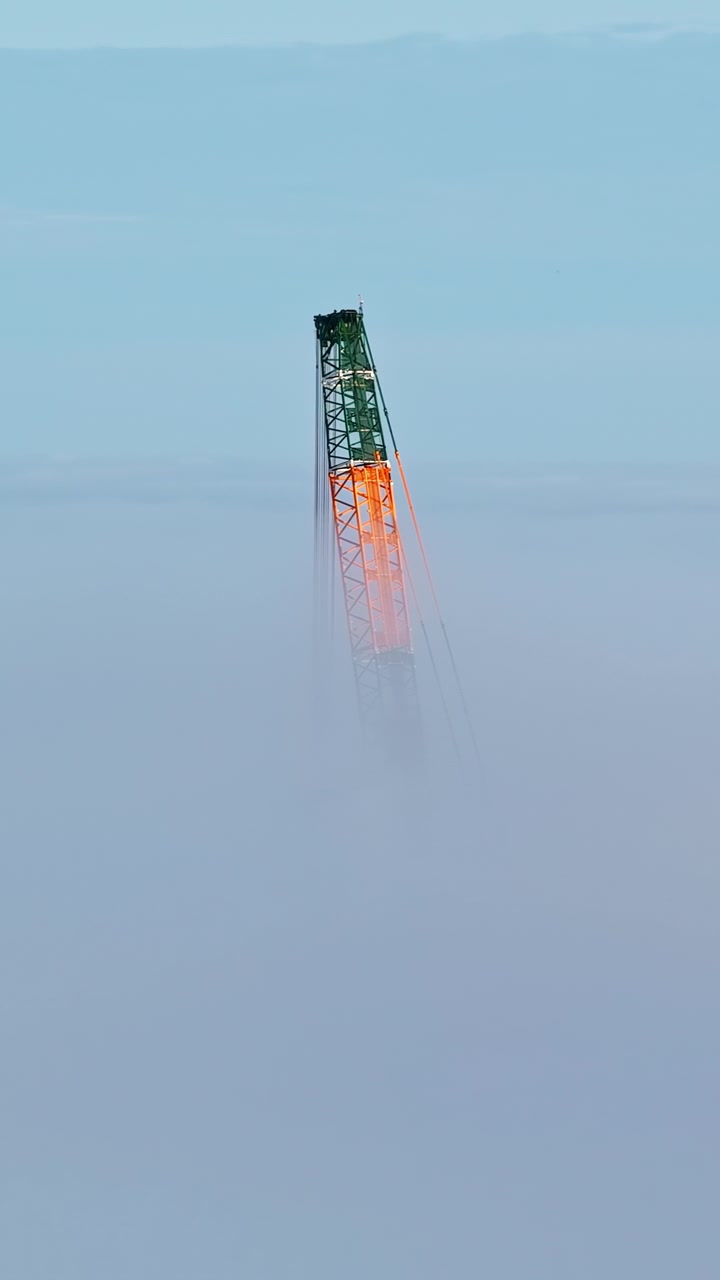 Crane tower top emerging through dense morning fog against a blue sky background