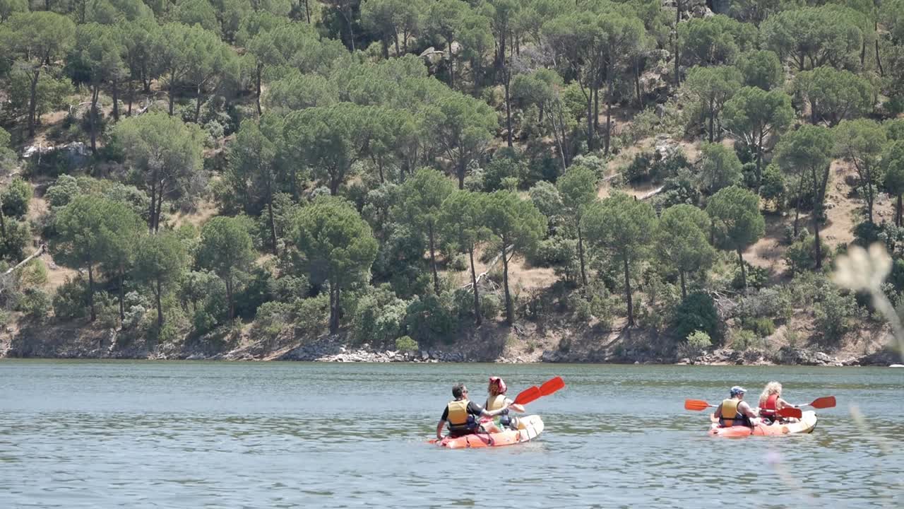 Due kayak con due persone ciascuno che remano in una giornata estiva attraverso le acque dolci del bacino idrico al Pantano de San Juan, Madrid