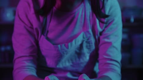 young woman potter working in the studio in neon lighting - puts her head up and looks in the camera