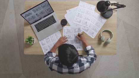 vista superior de un artista masculino asiático mirando el concepto de dibujo en una computadora portátil y dibujando el guión gráfico en la mesa con auriculares en el estudio
