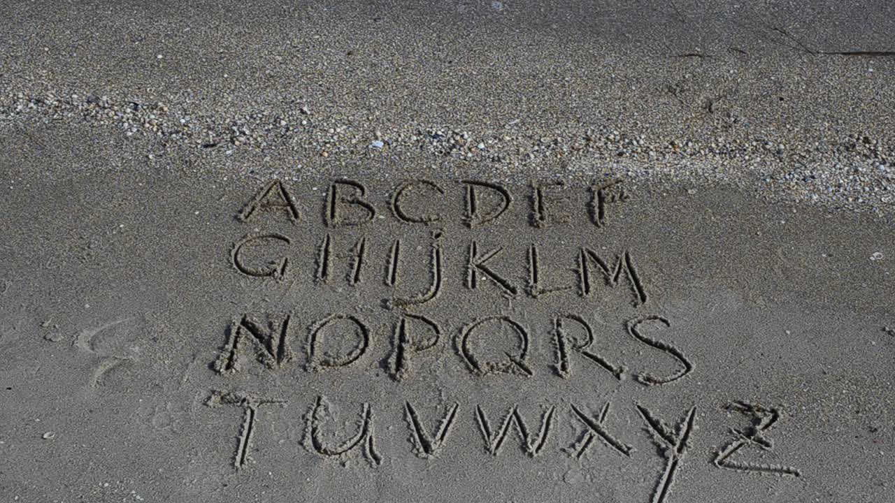 Alfabeto inglese scritto sulla sabbia della spiaggia. Ripresa sulla spiaggia