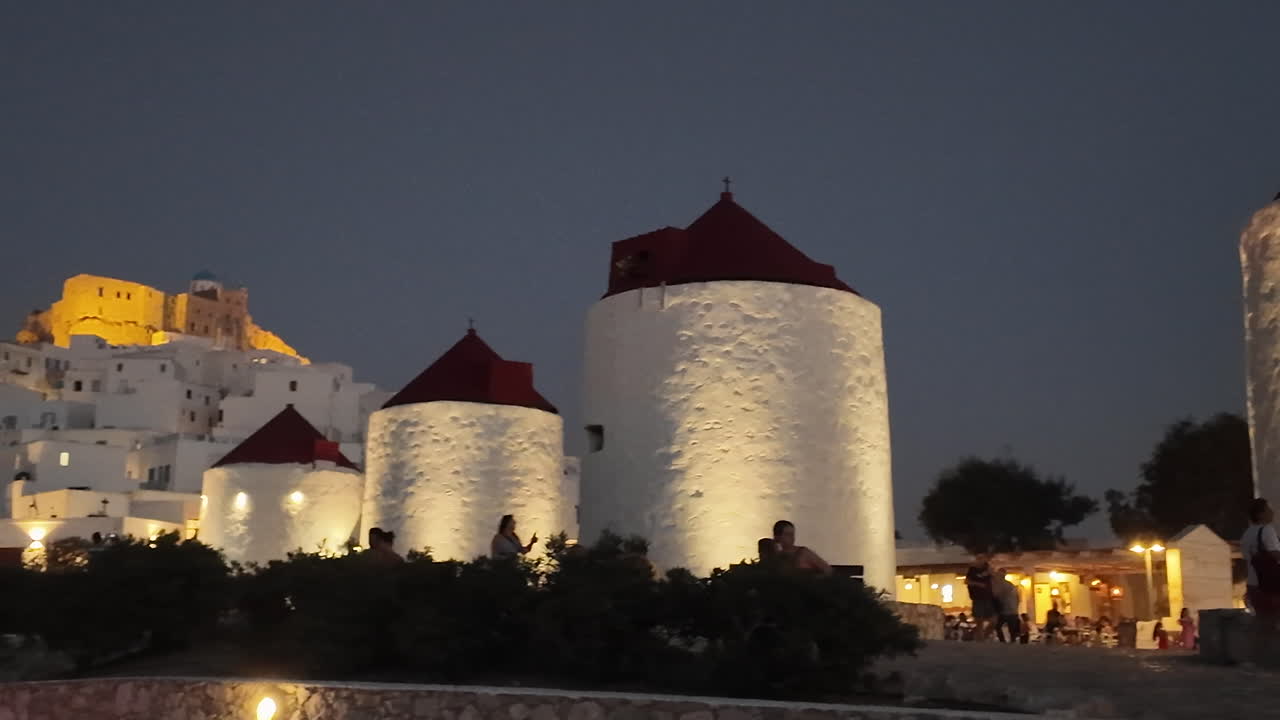 Greece, Astypalea Island, iconic windmills and castle nicely lighted up at night time.People walking and socializing around the windmills. Footage ends at the beautiful castle lighted up at the hill.