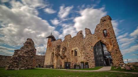 the ruins of the castle of dobele against a blue sky and white clouds