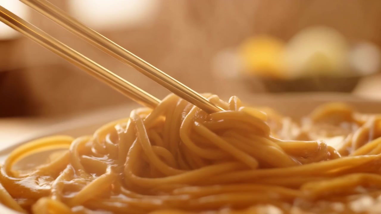 Noodles presi con le bacchette, in una ciotola di noodles su un tavolo, con bacchette, ciotola di noodles, da una ripresa ravvicinata dall'alto della ciotola, con accenti marroni e gialli