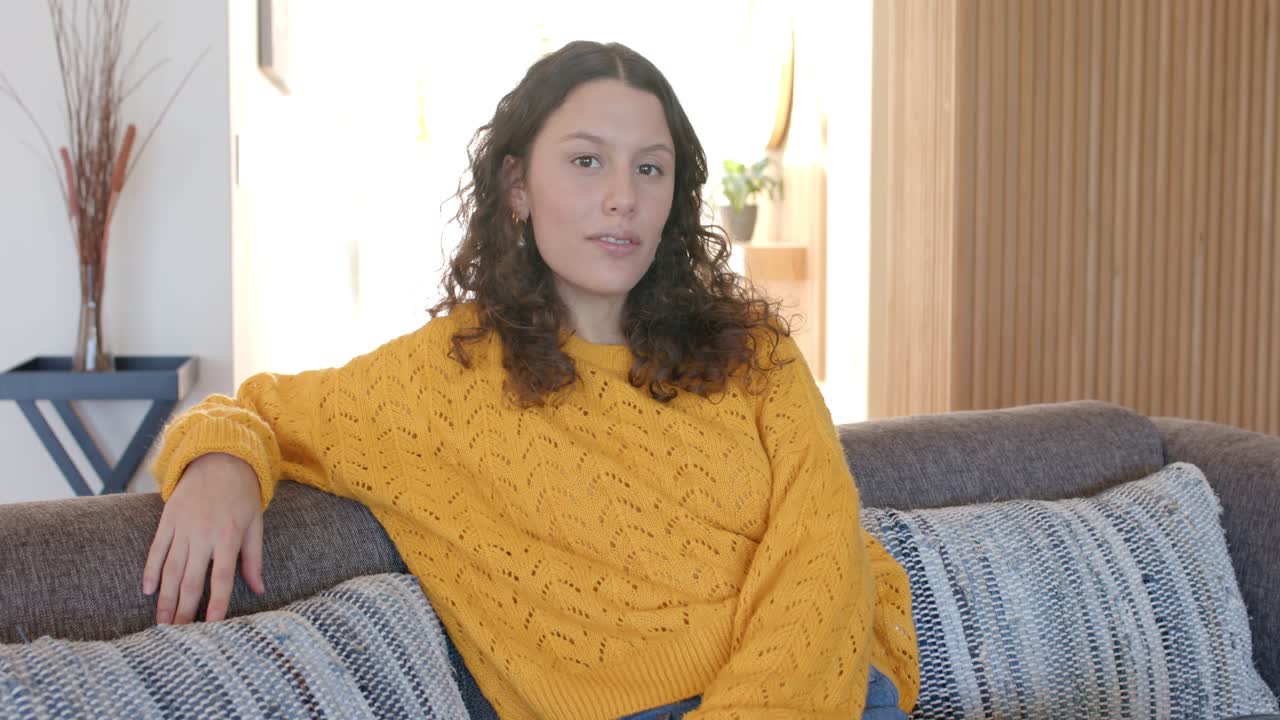 Camera zooming in capturing woman speaking shifting posture expressing ideas on sofa in living room