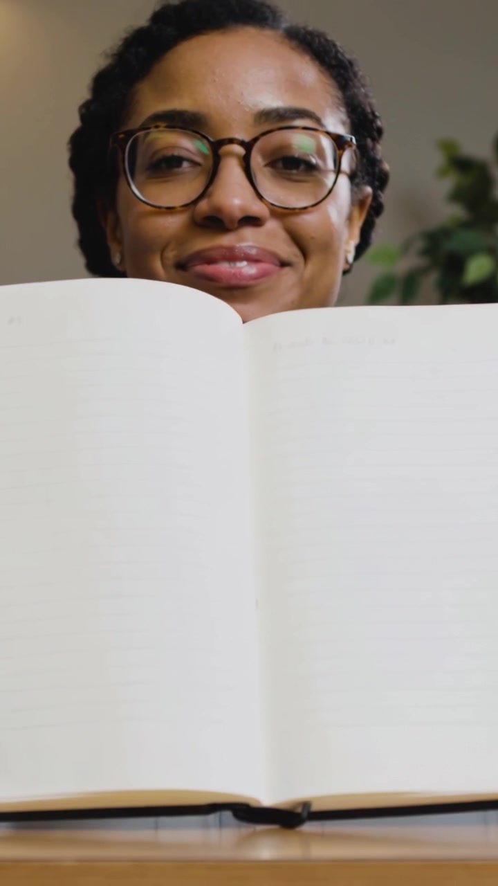 Video verticale: Sfogliare le pagine, donna in jeans con gli occhiali che apre un quaderno alla scrivania, mostrando le pagine