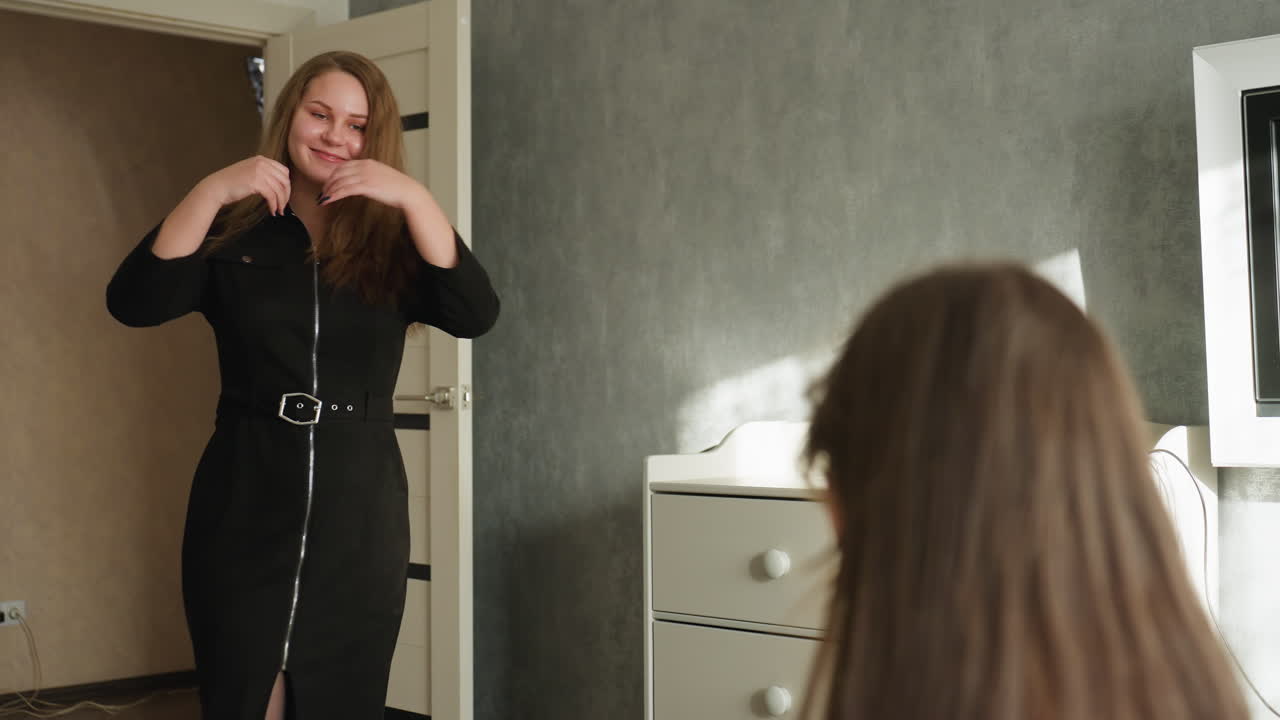 Amiche in una camera da letto moderna: una seduta sul letto, l'altra entra gioiosamente dalla porta, si gira mostrando un abito nero, lunghi capelli fluenti, sorridendo mentre l'amica la elogia, calda luce del giorno
