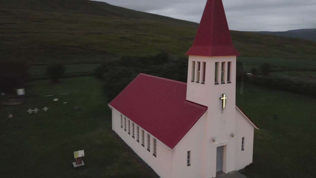In 4K, a solitary white church with a red roof called Lauf&aacute;skirkja stands in stark beauty against Iceland's sparse grasslands, a colonial beacon in a quaint town setting