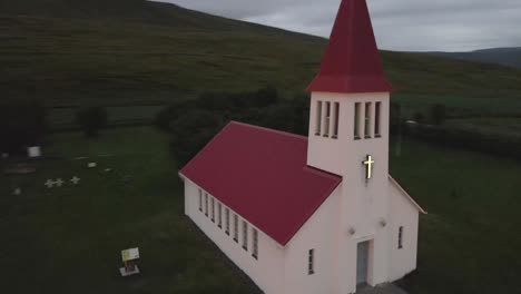 In-4K-Erhebt-Sich-Eine-Einsame-Weiße-Kirche-Mit-Rotem-Dach-Namens-Laufáskirkja-In-Schlichter-Schönheit-Vor-Den-Kargen-Graslandschaften-Islands,-Ein-Leuchtturm-Aus-Der-Kolonialzeit-In-Einer-Malerischen-Stadtkulisse