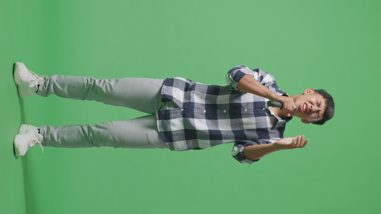 Full Body Of Young Asian Teen Boy Holding A Microphone And Singing On The The Green Screen Background