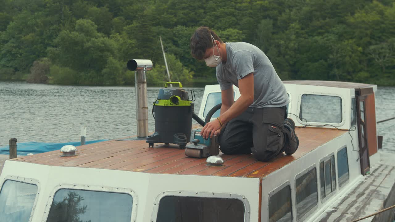젊은 남자가 나무 보트 선실에서 광택제를 제거하는 작업을 시작합니다.