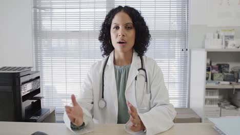 Biracial-female-doctor-sitting-at-desk-and-having-video-call,-slow-motion