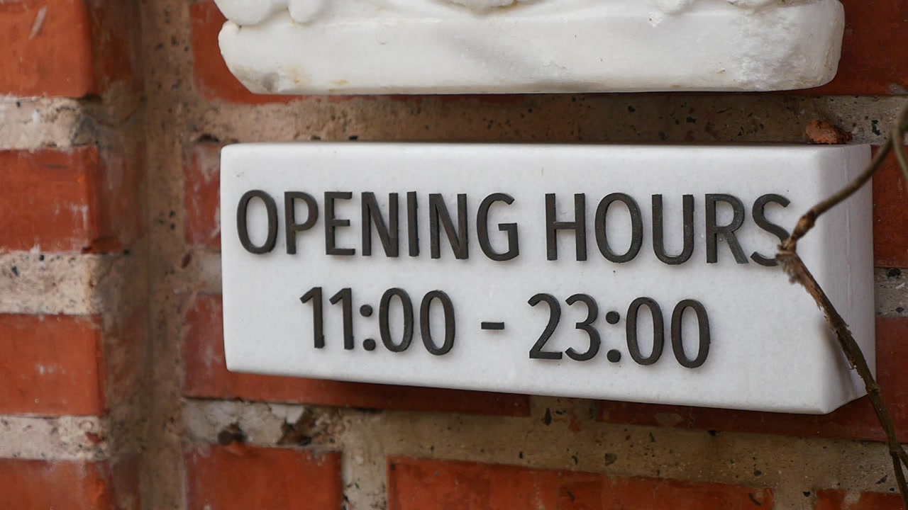 Close-up of a White Opening Hours Sign on a Brick Wall