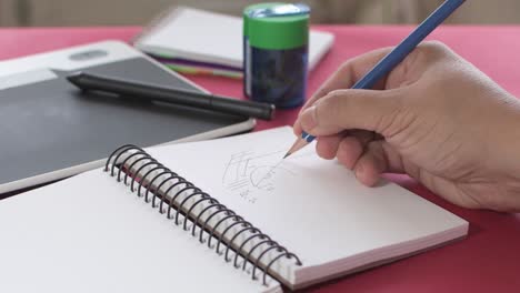 Woman's hands taking notes with a pencil in a notebook, together with a pencil sharpener and graphic tablet in the background.