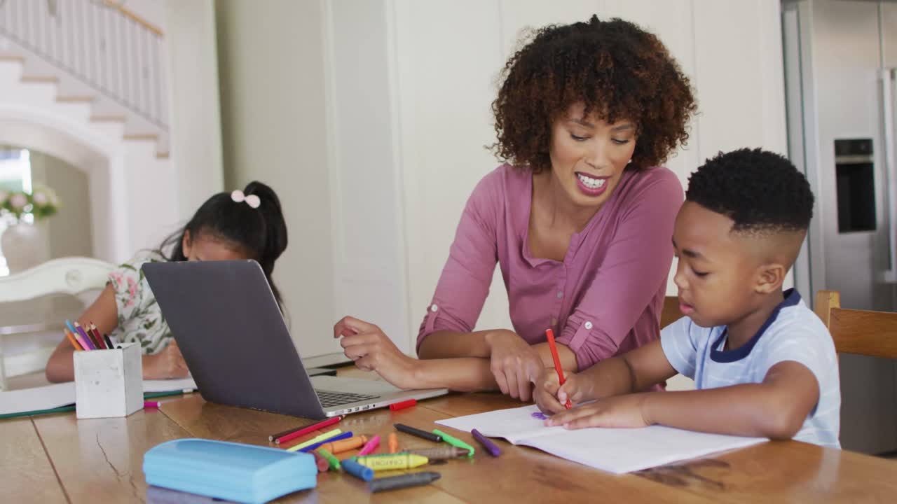 madre afroamericana, hija e hijo sentados en la mesa de la cocina haciendo la tarea