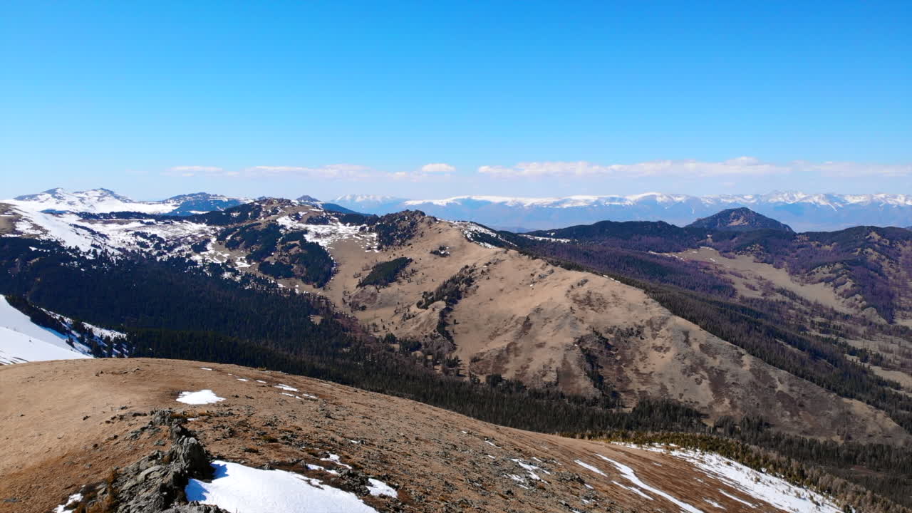 Panoramic view of a mountain range with snow patches and clear blue sky
