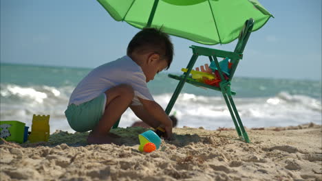 slow motion of a young brunette latin hispanic boy playing on the sand with his toys alone on a windy sunny day at the mayan riviera