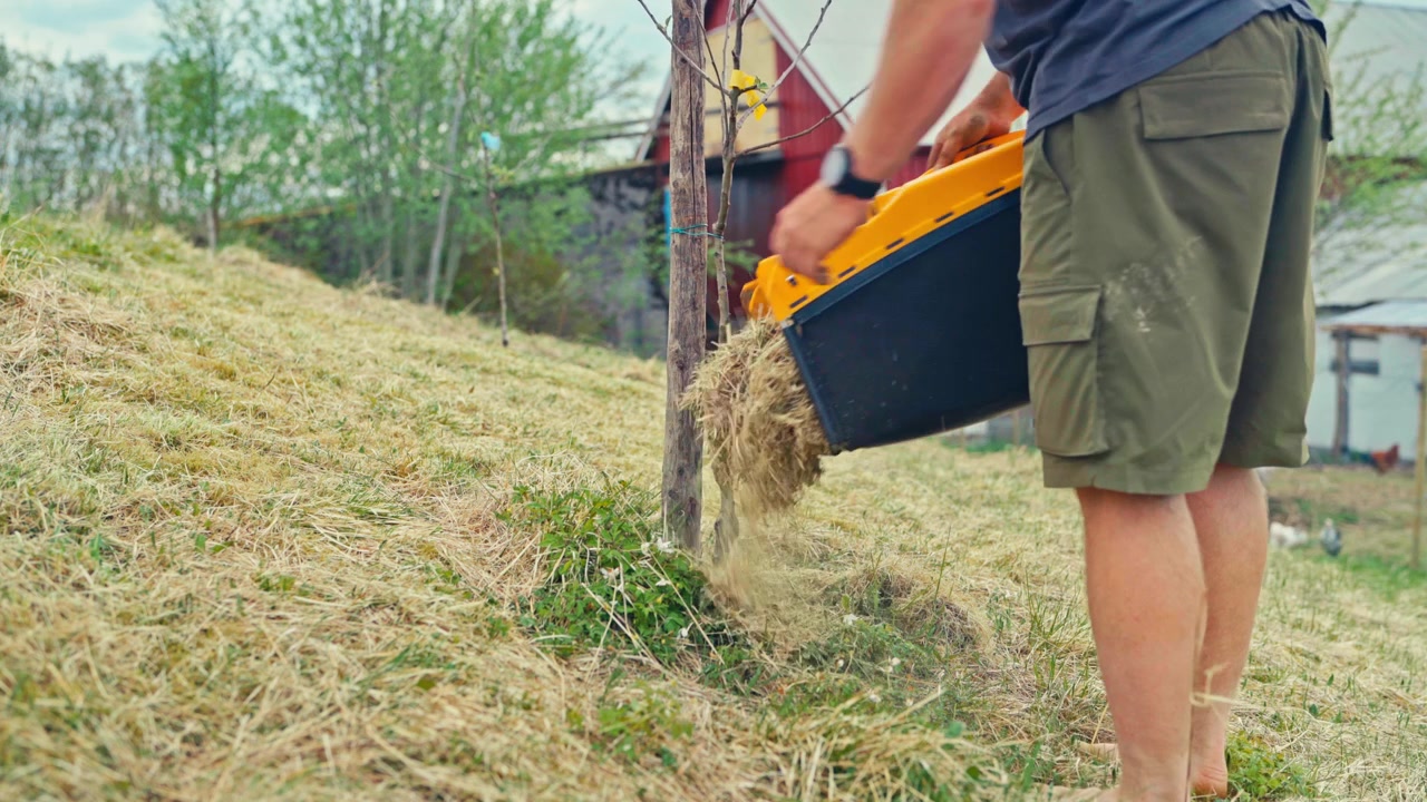 A man cleans out freshly cut straw and grass clippings stuck inside a lawn mower during yard work