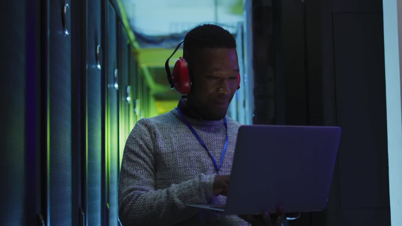 African american male computer technician using laptop working in business server room