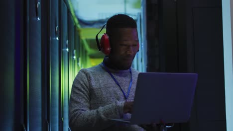 técnico informático afroamericano que usa una computadora portátil trabajando en una sala de servidores de negocios