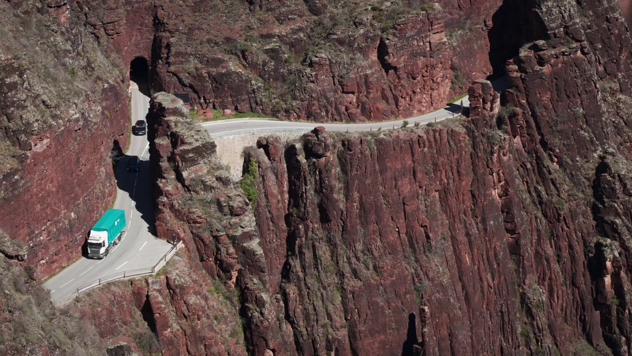 Primo piano della strada attraverso le Gole del Daluis (Gorges de Daluis) in Francia. Un camion sta emergendo da un tunnel molto piccolo. Diverse auto lo seguono. La strada costeggia il ripido bordo della scogliera