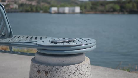 un teléfono negro se sienta en un banco gris junto a un lago