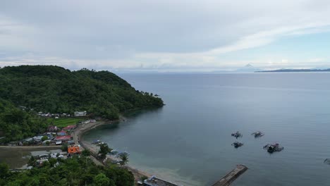 Breathtaking-Aerial-Orbit-of-Quaint,-Rural-Fishing-Village-facing-calm-Ocean-Waters-and-stunning-cloudscape-in-Catanduanes,-Philippines