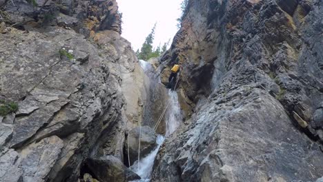 Hombre-En-Traje-De-Neopreno-Hace-Rappel-En-La-Cascada-Del-Cañón-Del-Río-Con-Un-Paquete-En-La-Espalda