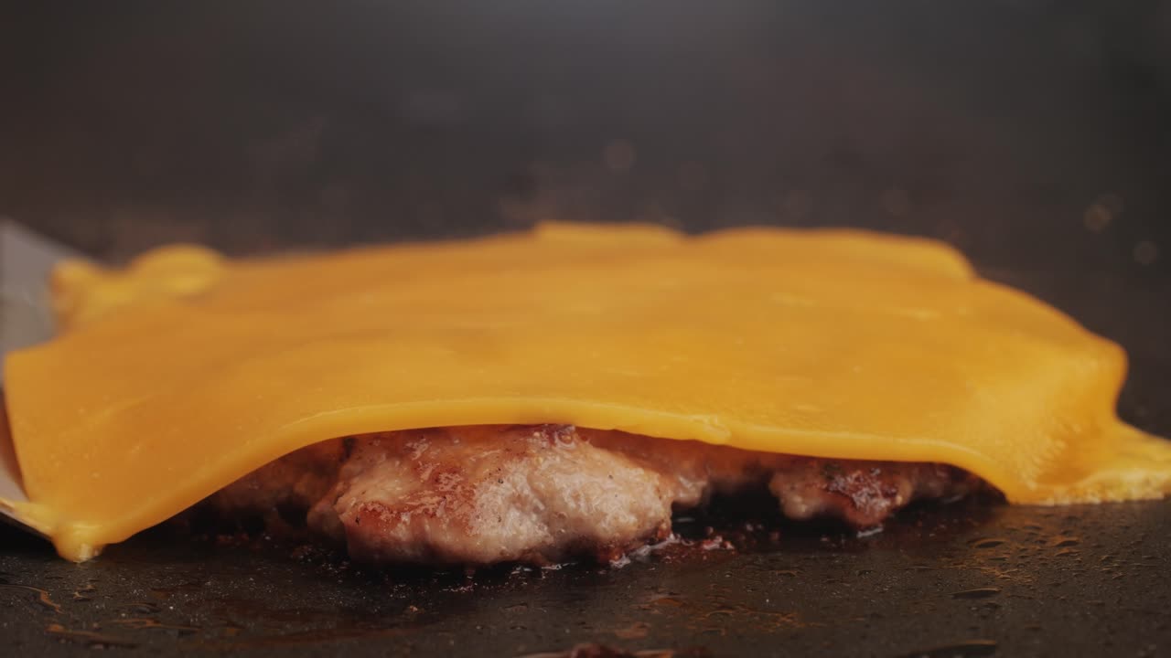 Cooking American fat smash burger with cheese slice on top on grill close-up. Beef or pork cutlet smashing by burger press. The chef in kitchen of the restaurant making cutlets for burgers - smash burger beefsteak. Fast and street food concept.