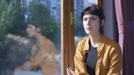 건강하지 않은 젊은 여성은 긴장을 풀기 위해 창문 밖을 바라보고 있습니다.