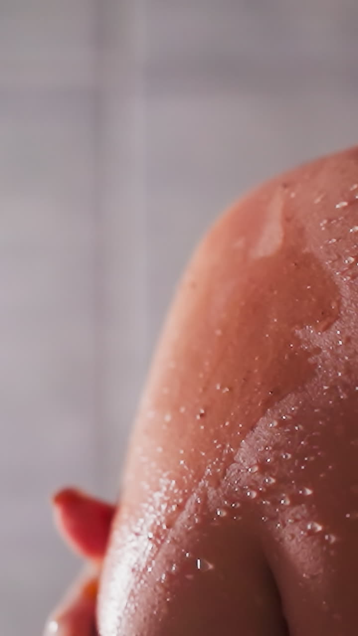 Woman applies scrub on shoulder in shower unit closeup. Lady exfoliates dry skin with homemade cosmetic product in bathroom. Spa relaxation at home