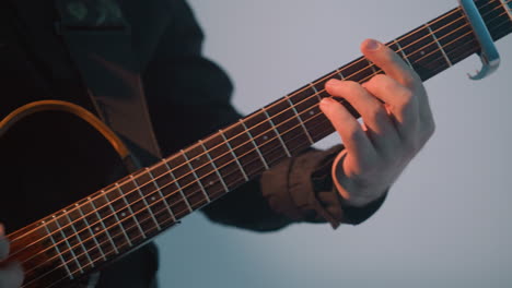 ein gesichtsloser gitarrist spielt eine gitarre vor einem weißen und blauen hintergrund. die nahaufnahme konzentriert sich auf die hände des musikers und die saiten der gitarre