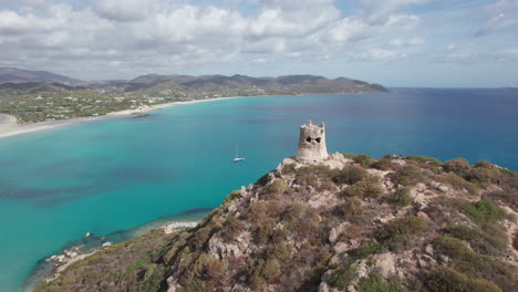 fantástica toma aérea en dirección a la torre di porto giunco en el cabo carbonara con la hermosa playa en el fondo