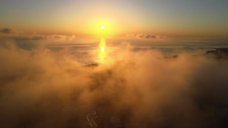 Aerial-seaside-sunrise-flying-out-of-clouds-in-Santorini-island,-Greece