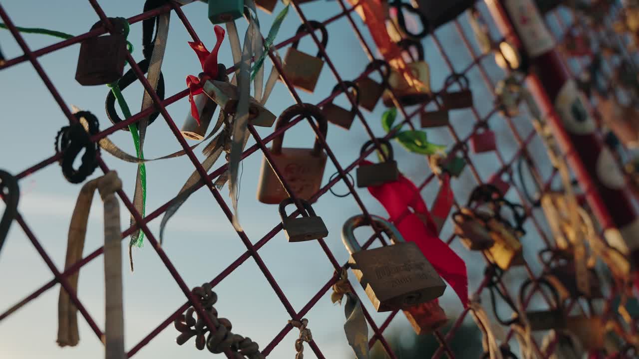Close up of colorful love locks and ribbons on a metal fence against a blue sky