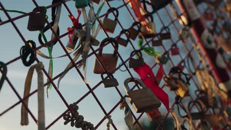 close up of colorful love locks and ribbons on a metal fence against a blue sky