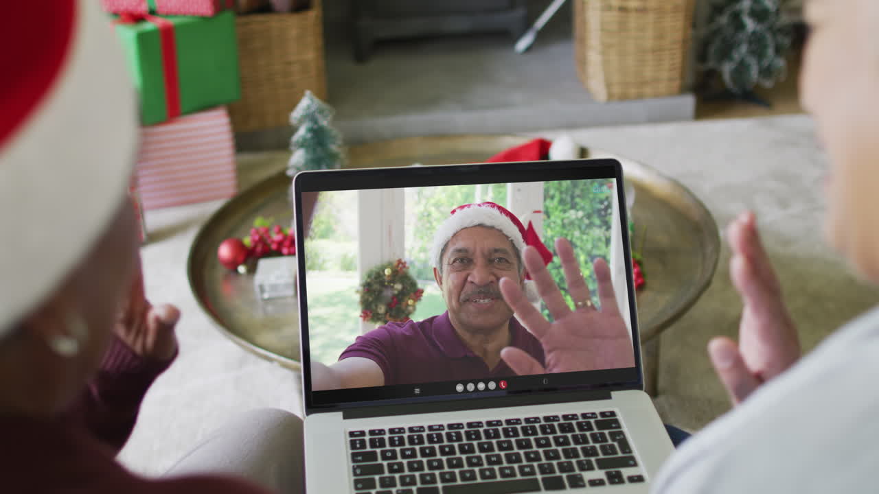 amigas mayores diversas usando una computadora portátil para una videollamada de navidad con una amiga sonriente en la pantalla