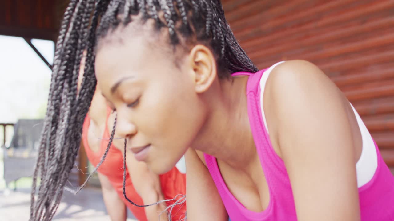 una feliz pareja afroamericana haciendo yoga y estirándose en una cabaña de madera, cámara lenta
