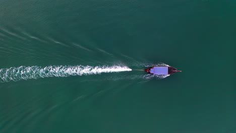 motor long-tail boat cruising in sea waters with kelvin wake behind