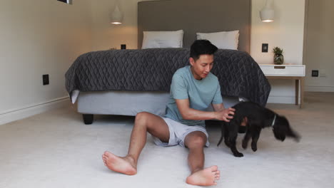 asian man playing with dog on bedroom floor, enjoying quality time together, at home