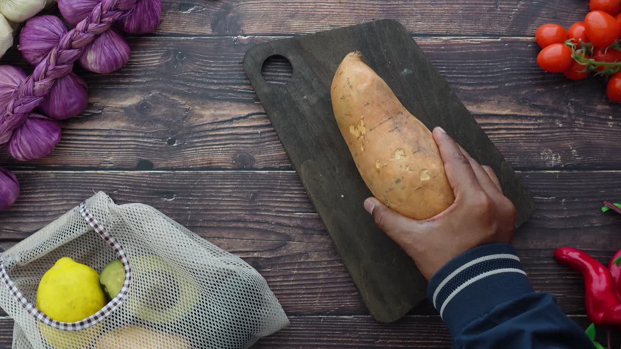 Mano che posiziona una patata dolce fresca su un tagliere di legno