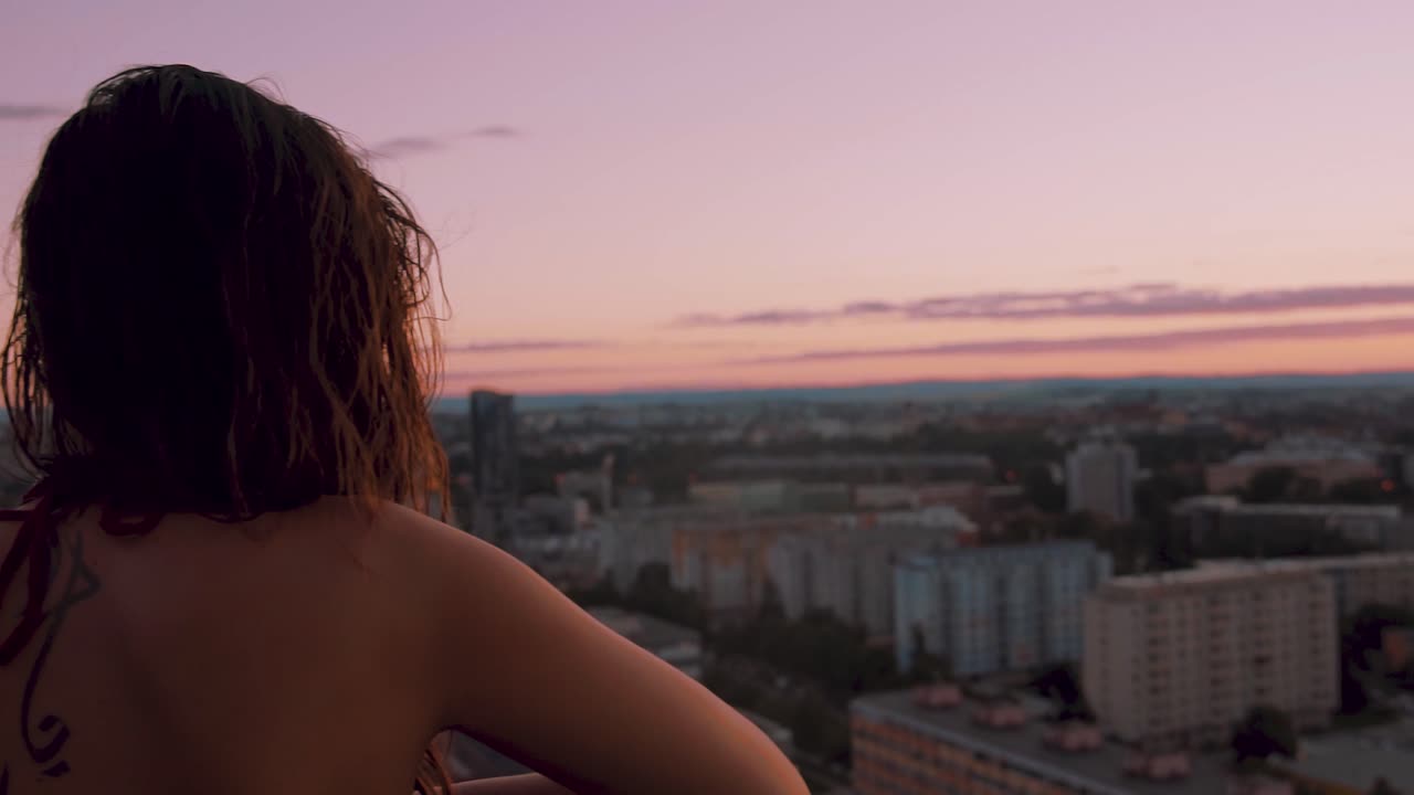 Panorama of beautiful sexy young girl, enjoying the majestic view of city from the high elevated balcony of hotel room. Sunset View from back