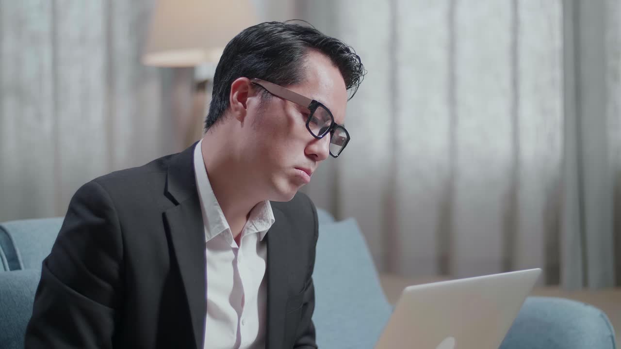 primer plano de un hombre de negocios asiático con chaqueta y pantalones cortos que tiene dolor de cabeza mientras trabaja con una computadora portátil en casa